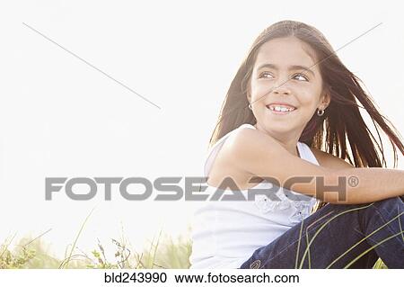 Stock Image - Wind blowing hair of Mixed Race girl sitting in grass. Fotosearch