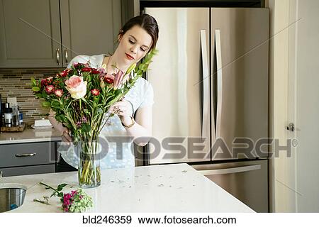Stock Photo - Woman arranging flowers in domestic kitchen. Fotosearch