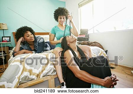 Woman braiding hair of friend in bedroom View Large Photo Image Stock Photo - Woman braiding hair of friend in bedroom. Fotosearch