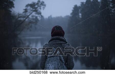 Woman carrying backpack standing near still lake View Large Photo Image Stock Photo - Woman carrying backpack standing near still lake. Fotosearch