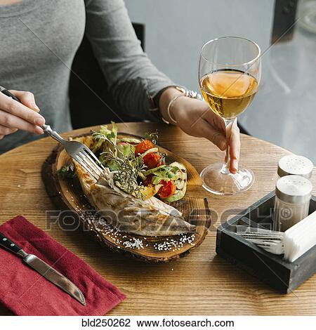 Stock Image - Woman eating fish with white wine. Fotosearch