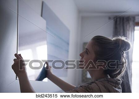 Stock Photography - Woman hanging painting on wall. Fotosearch