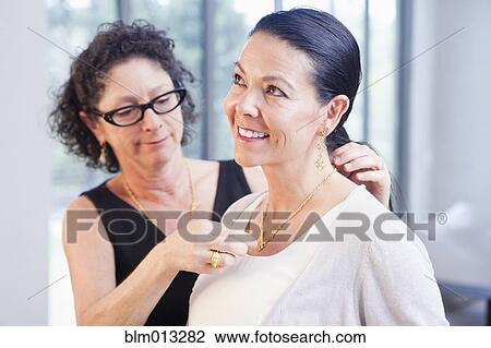 Stock Image - Woman helping customer put on necklace in jewelry store. Fotosearch