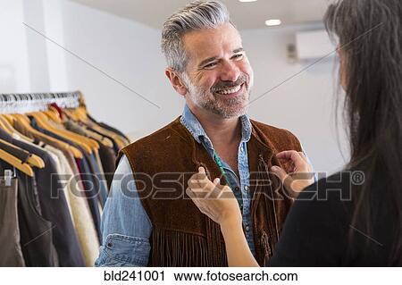 Stock Image - Woman helping man with fringe vest in store. Fotosearch