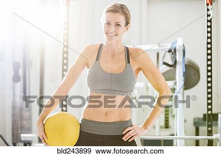 Stock Photo - Woman holding heavy ball in gymnasium. Fotosearch
