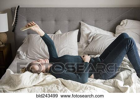 Stock Photo - Woman laying on bed posing for cell phone selfie. Fotosearch