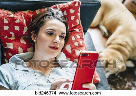 Woman laying on sofa near dog texting on cell phone View Large Photo Image Picture - Woman laying on sofa near dog texting on cell phone. Fotosearch