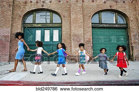 Woman leading girls holding hands on city sidewalk View Large Photo Image Stock Photograph - Woman leading girls holding hands on city sidewalk. Fotosearch