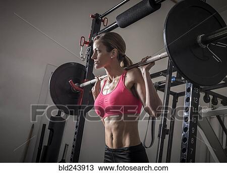 Stock Image - Woman lifting barbell in gymnasium. Fotosearch