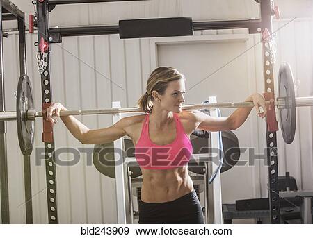 Stock Photo - Woman lifting barbell in gymnasium. Fotosearch