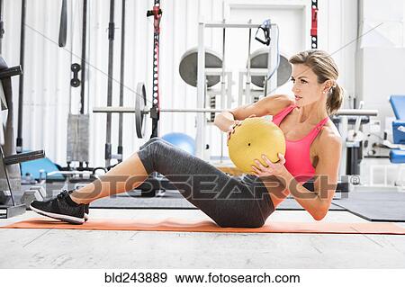 Stock Photo - Woman lifting heavy ball on exercise mat in gymnasium. Fotosearch