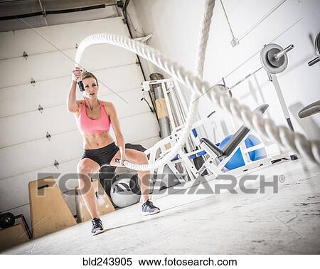 Stock Photography - Woman lifting heavy ropes in gymnasium. Fotosearch