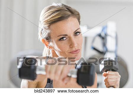Stock Photo - Woman lifting weights in gymnasium. Fotosearch