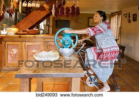 Stock Image - Woman pedaling to power grinder in kitchen. Fotosearch