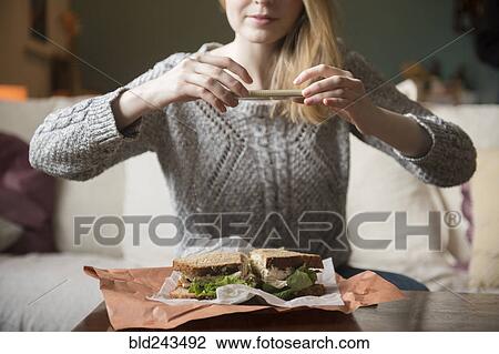 Stock Image - Woman photographing sandwich with cell phone. Fotosearch