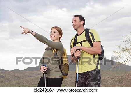 Stock Photo - Woman pointing to man in desert while hiking. Fotosearch