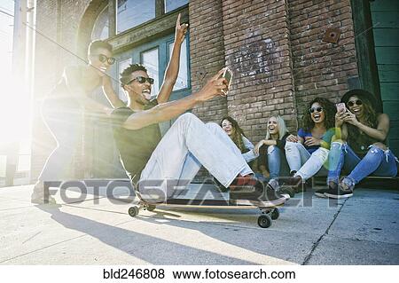 Woman pushing friend sitting on skateboard in city View Large Photo Image Stock Photo - Woman pushing friend sitting on skateboard in city. Fotosearch