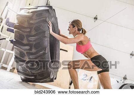 Woman pushing heavy tire in gymnasium View Large Photo Image Stock Photograph - Woman pushing heavy tire in gymnasium. Fotosearch