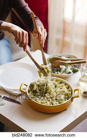 Stock Image - Woman serving pasta with wooden spoons. Fotosearch