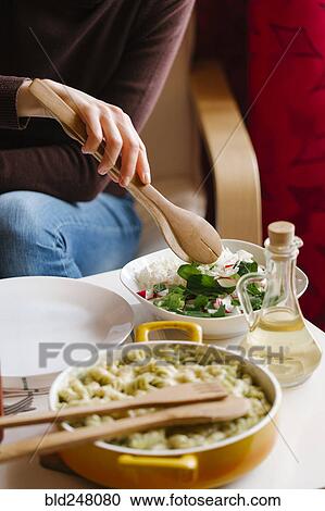Stock Image - Woman serving salad with wooden tongs. Fotosearch