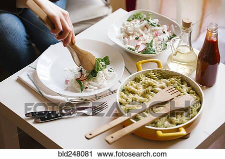 Stock Image - Woman serving salad with wooden tongs. Fotosearch