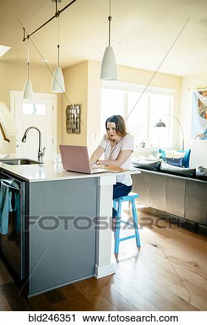 Stock Image - Woman sitting at counter using laptop. Fotosearch
