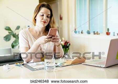 Stock Photo - Woman sitting at table texting on cell phone. Fotosearch