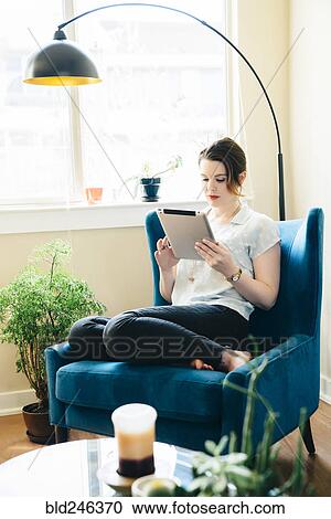Woman sitting in armchair using digital tablet View Large Photo Image Stock Image - Woman sitting in armchair using digital tablet. Fotosearch