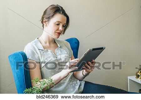 Woman sitting in armchair using digital tablet View Large Photo Image Stock Photo - Woman sitting in armchair using digital tablet. Fotosearch