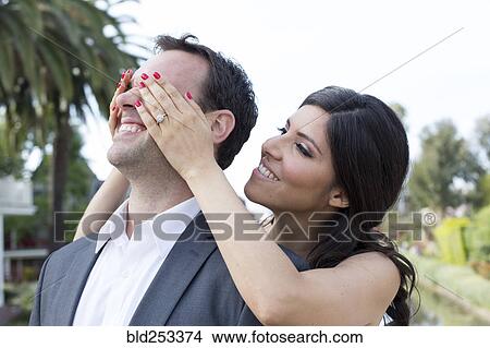 Woman standing behind man covering his eyes View Large Photo Image Picture - Woman standing behind man covering his eyes. Fotosearch