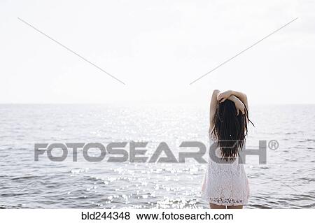 Woman standing near ocean with arms raised View Large Photo Image Stock Photo - Woman standing near ocean with arms raised. Fotosearch