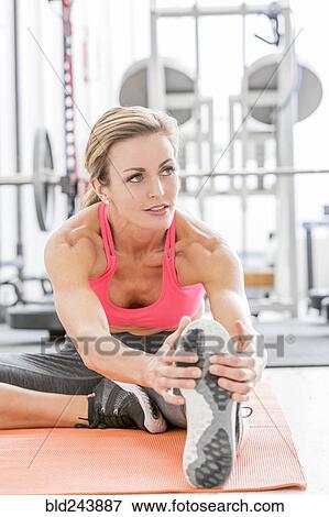 Woman stretching leg on exercise mat in gymnasium View Large Photo Image Stock Photo - Woman stretching leg on exercise mat in gymnasium. Fotosearch