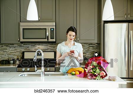 Woman texting on cell phone in domestic kitchen View Large Photo Image Stock Photo - Woman texting on cell phone in domestic kitchen. Fotosearch