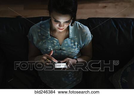 Picture - Woman texting on cell phone in the dark. Fotosearch