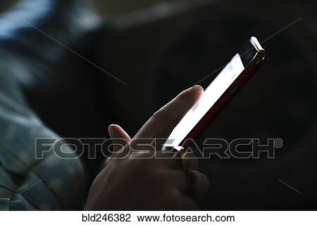 Stock Image - Woman texting on cell phone in the dark. Fotosearch
