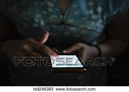Stock Image - Woman texting on cell phone in the dark. Fotosearch