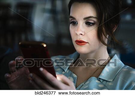 Stock Photo - Woman texting on cell phone in the dark. Fotosearch