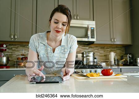 Woman using digital tablet and chopping food in domestic kitchen View Large Photo Image Picture - Woman using digital tablet and chopping food in domestic kitchen. Fotosearch