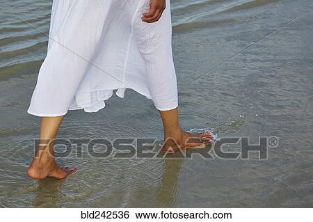 Stock Photograph - Woman wading barefoot in ocean. Fotosearch
