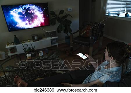 Stock Photograph - Woman watching television and using cell phone. Fotosearch