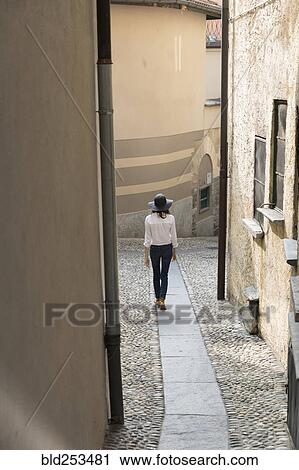 Woman wearing sun hat walking on narrow sidewalk View Large Photo Image Stock Image - Woman wearing sun hat walking on narrow sidewalk. Fotosearch