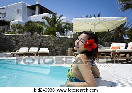 Stock Image - Woman with flower in hair relaxing in swimming pool. Fotosearch