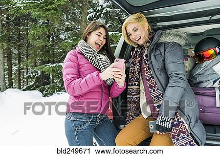 Stock Image - Women at car posing for cell phone selfie in winter. Fotosearch