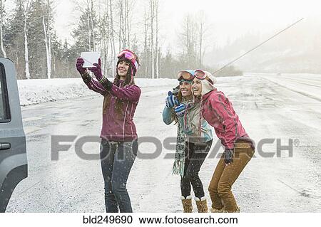 Stock Image - Women posing for cell phone selfie in winter using digital tablet. Fotosearch