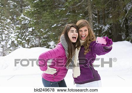 Stock Photo - Women posing for cell phone selfie in winter. Fotosearch