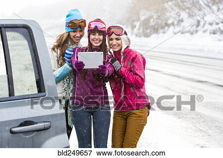 Stock Photo - Women posing for selfie with digital tablet near car in winter. Fotosearch