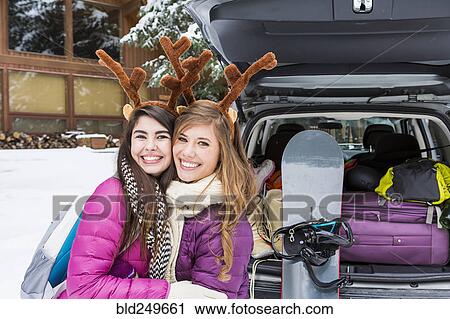 Stock Image - Women posing near car in winter wearing toy antlers. Fotosearch