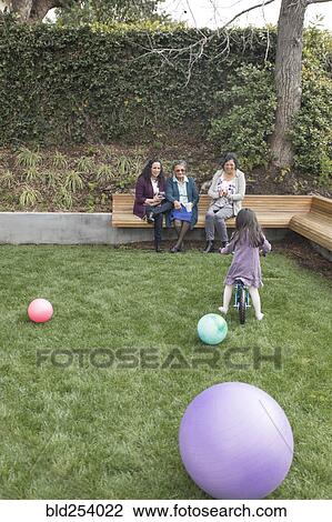 Stock Image - Women watching girl riding bicycle in grass. Fotosearch