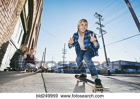 Stock Photo - Women watching man skateboarding on urban sidewalk. Fotosearch