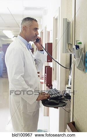 Stock Photo - African American doctor using equipment and talking on telephone in hospital. Fotosearch